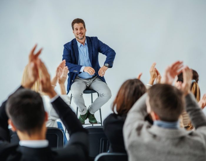 Smiling Motivational Speaker in Front of Clapping Audience